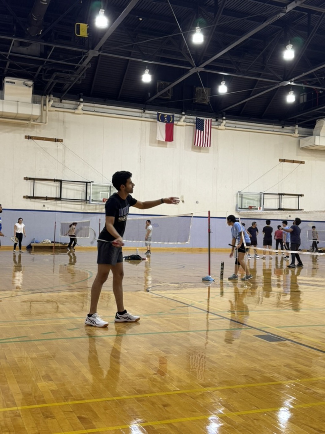 Ribhav mid-serve on an indoor badminton court