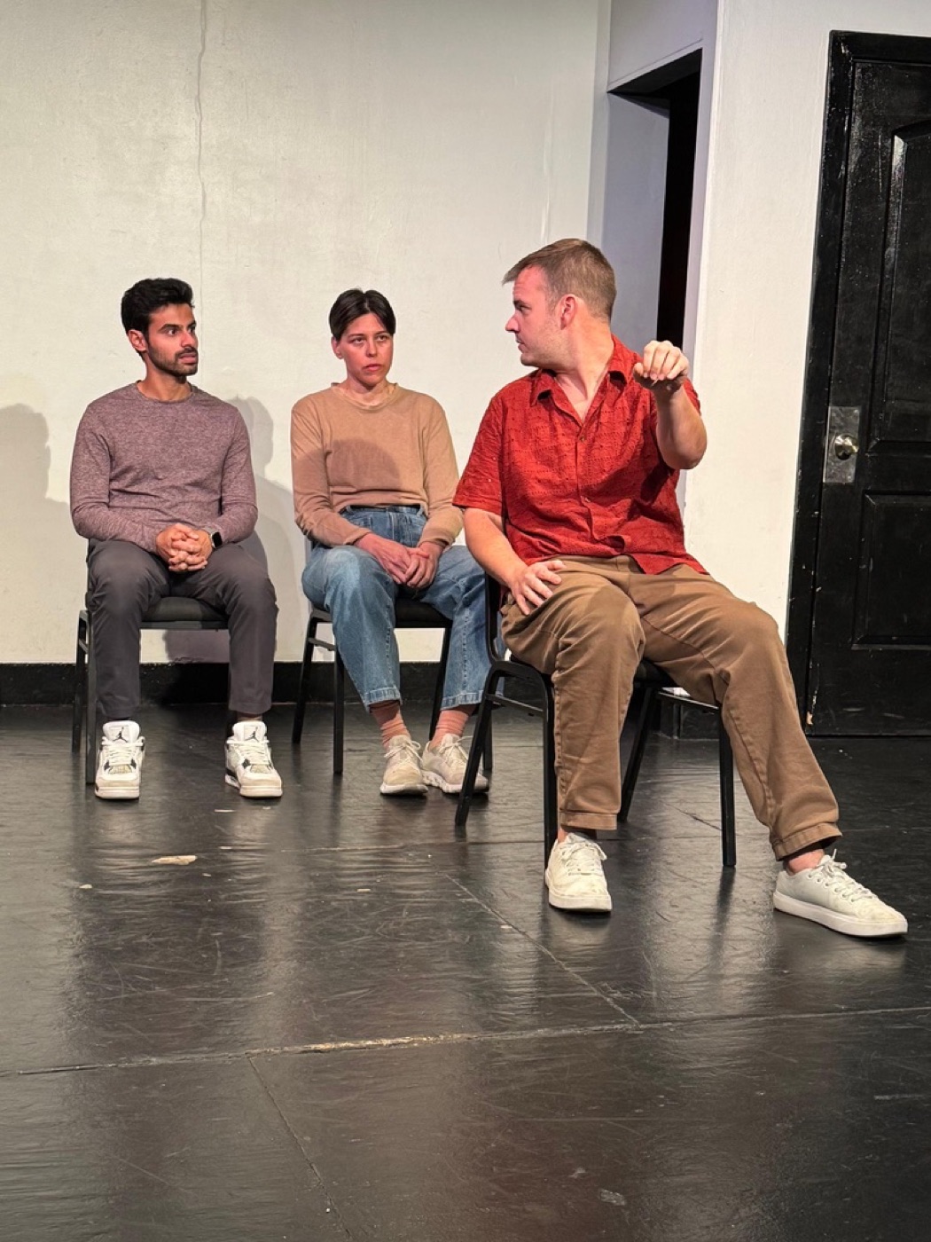 Ribhav performing improv on stage, seated with two other actors